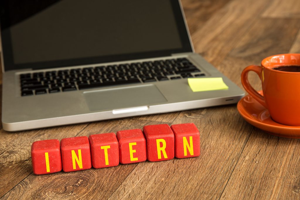 Intern written on a wooden cube in front of a laptop.